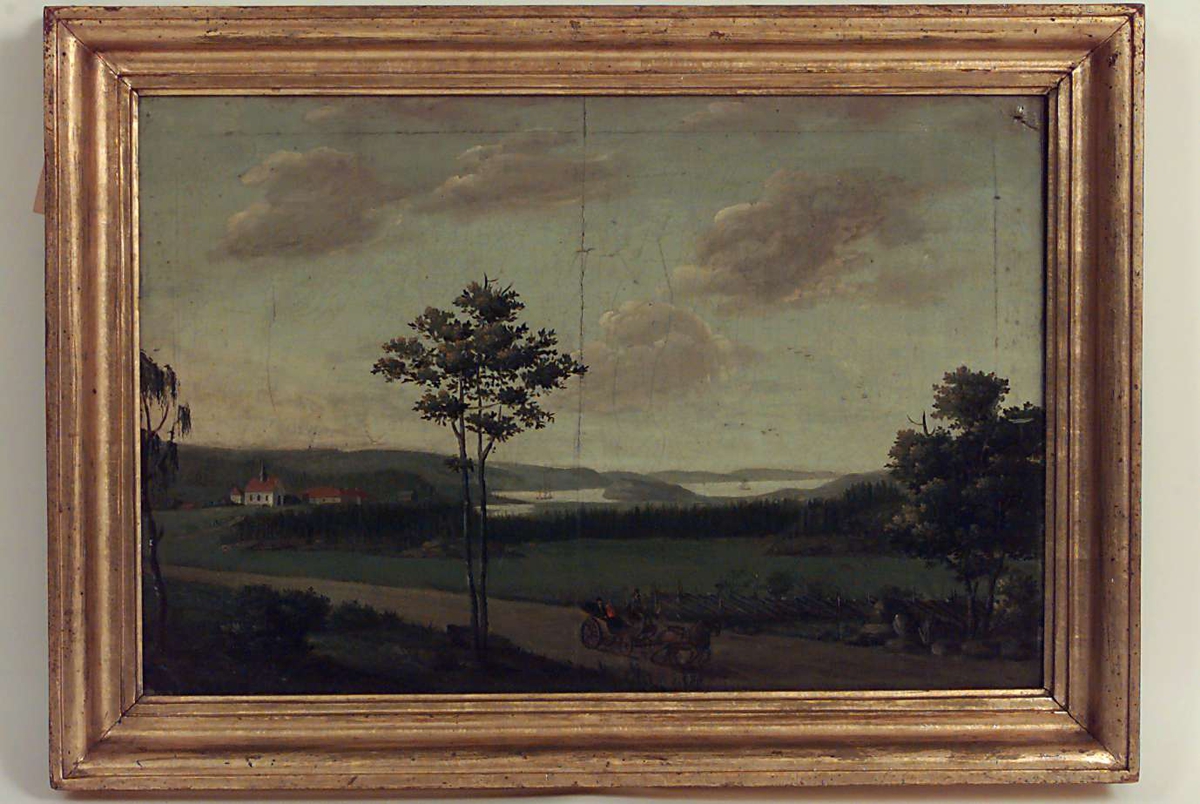 Skjeberg prestegård og kirke, i forgrunnen landevei med kjøretøy. 
