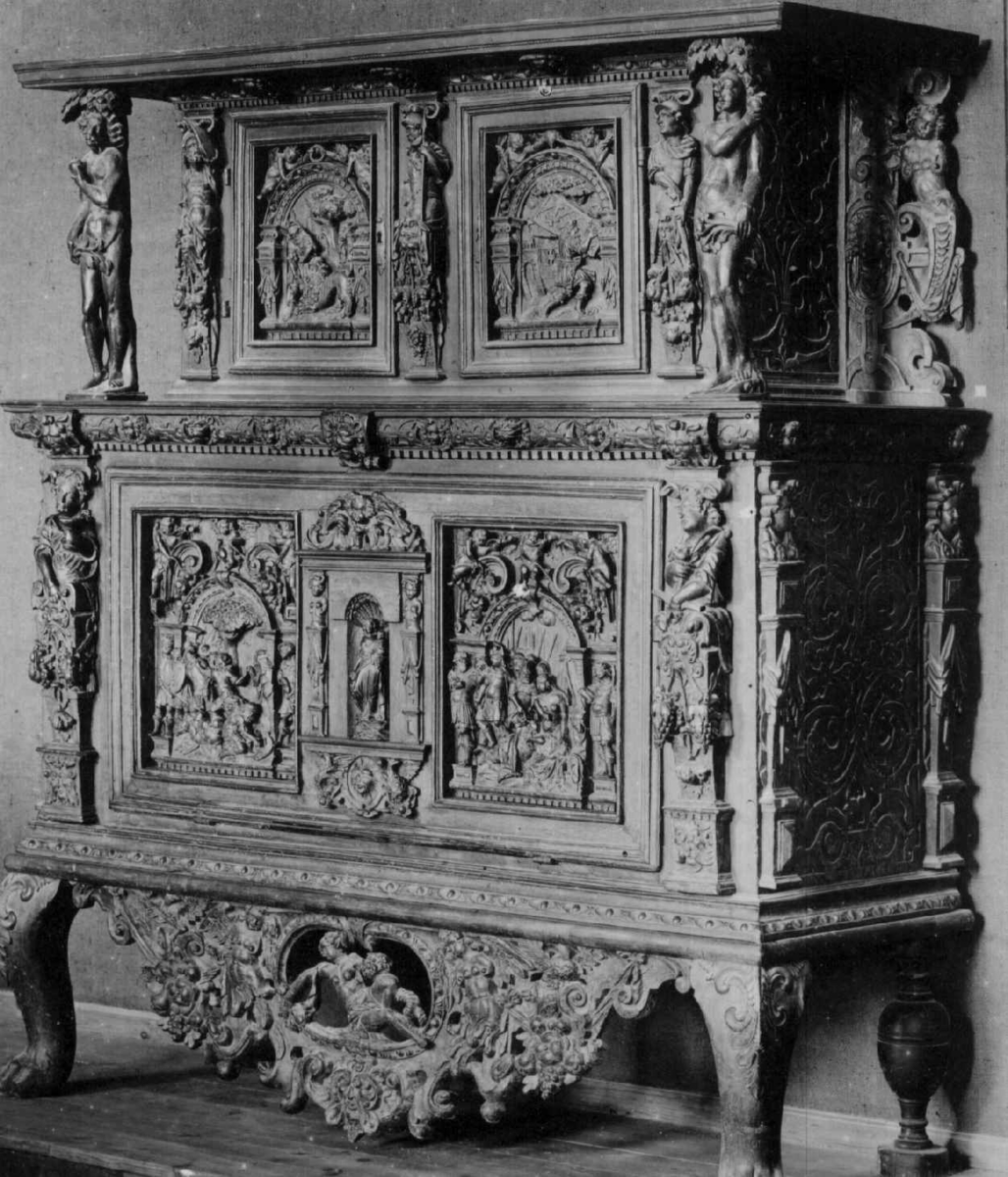 Rektangulært skap med skåret ornamentikk i flere deler. Øvre skap med to dører og gesims. Nedre skap med en klaff fremstilt som to dører. Skapdelene står på en sokkel med fire ben. Tympanon på øvre skap. Skapet ble opprinnelig brukt som skjenk med åpen klaff for å servere drikkevarer til gjester.
På overskapet i dørfyllinger er utskåret motiv fra gamle testament: "Samsons kamp med løven" og "Samson bærer bort Gazas byport". På underskap i fyllinger: "Samson slår filisterne med asenkjeven" og "Samson og Dalila". Dørene blir flankert av hermenpilaster. Mellom fyllinger på overskap aedikula med dyden "kjærlighet".  Som karyatide og atlant to utskårete figuerer "Adam og Eva" ved overskap. 
Klassiske profiler med eggstav, perlestav og tannsnitt. Beslagverkornament på skapsidene, gesimsens underside og profil på underskap. 
Utskårete hoder av løver, engler, kvinner, masker på gesimsens underside og profil på underskap. Sidebrett med hermer, portretter i medaljonger og beslagverk. Sokkelen består av dreide og utskårete ben, holdt av en ramme, Forsidens blending er dekorert med utskårete figurer og ornamenter i ørebruskstil.
Flere deler er sekundære.