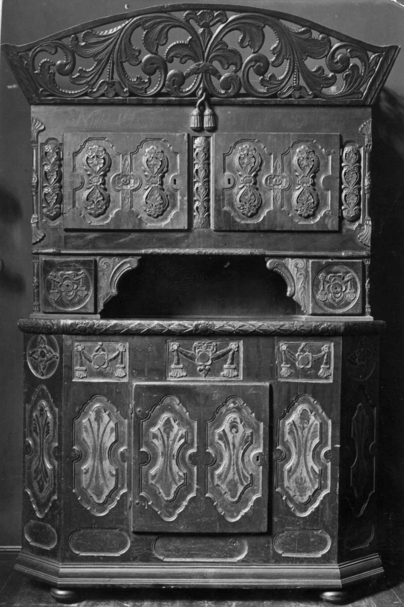 Framskap på fire dreide ben. Dekorert med marmorering, utskårne klassisistiske motiv og krone med gjennombrutt akantusranke.