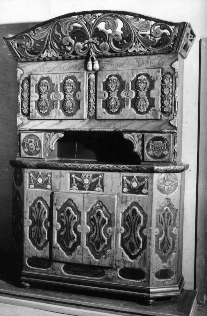 Framskap på fire dreide ben. Dekorert med marmorering, utskårne klassisistiske motiv og krone med gjennombrutt akantusranke.