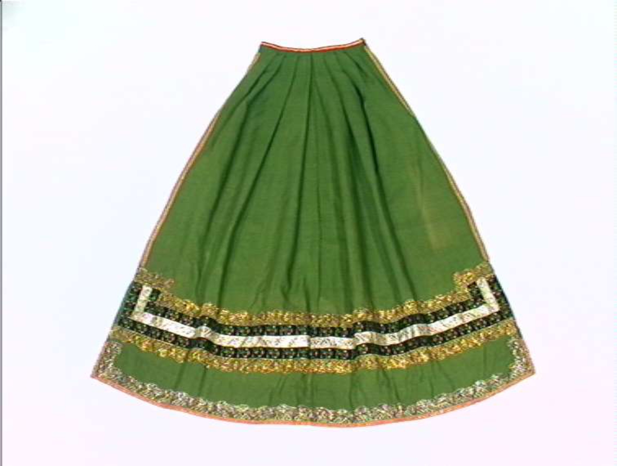 Grønt forkle av ull med dekor av metallblonder og bånd.