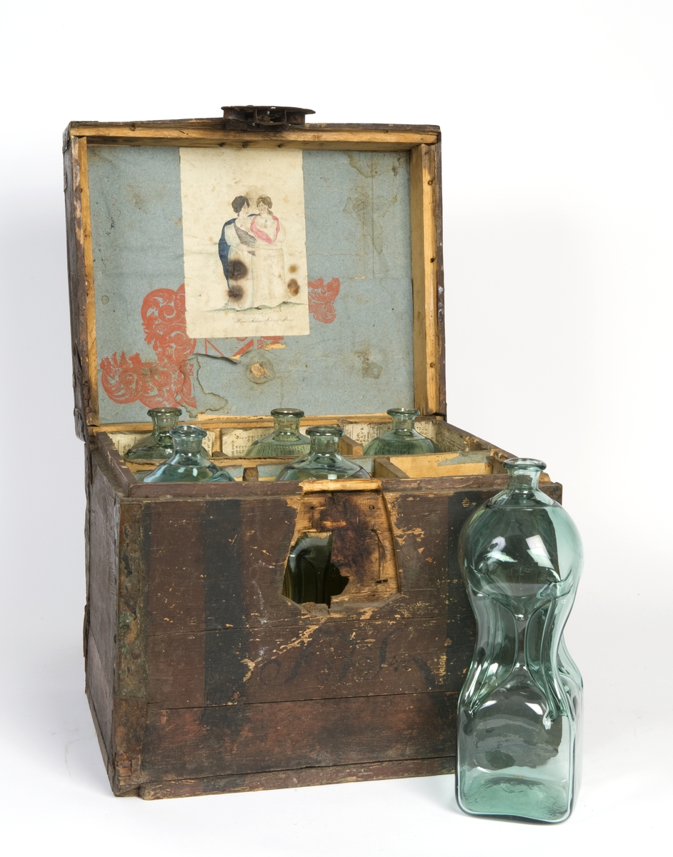 Trekasse med 6 glassflasker og rom i midten for glass. Gamle kalenderblader fra 1824 klistret inni. I lokket klistret en tegning av to damer, vannfarge, signert Hans Johan Fredrich Berg. Lokket foret med grått papir, delvis med rødt trykt mønster.