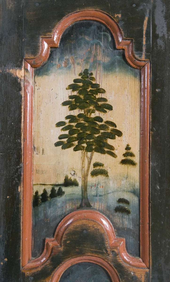 Flatskap med doble dører og klaff i overkant, hengslet på undersiden. Dekormalt med landskapsmotiver i feltene.