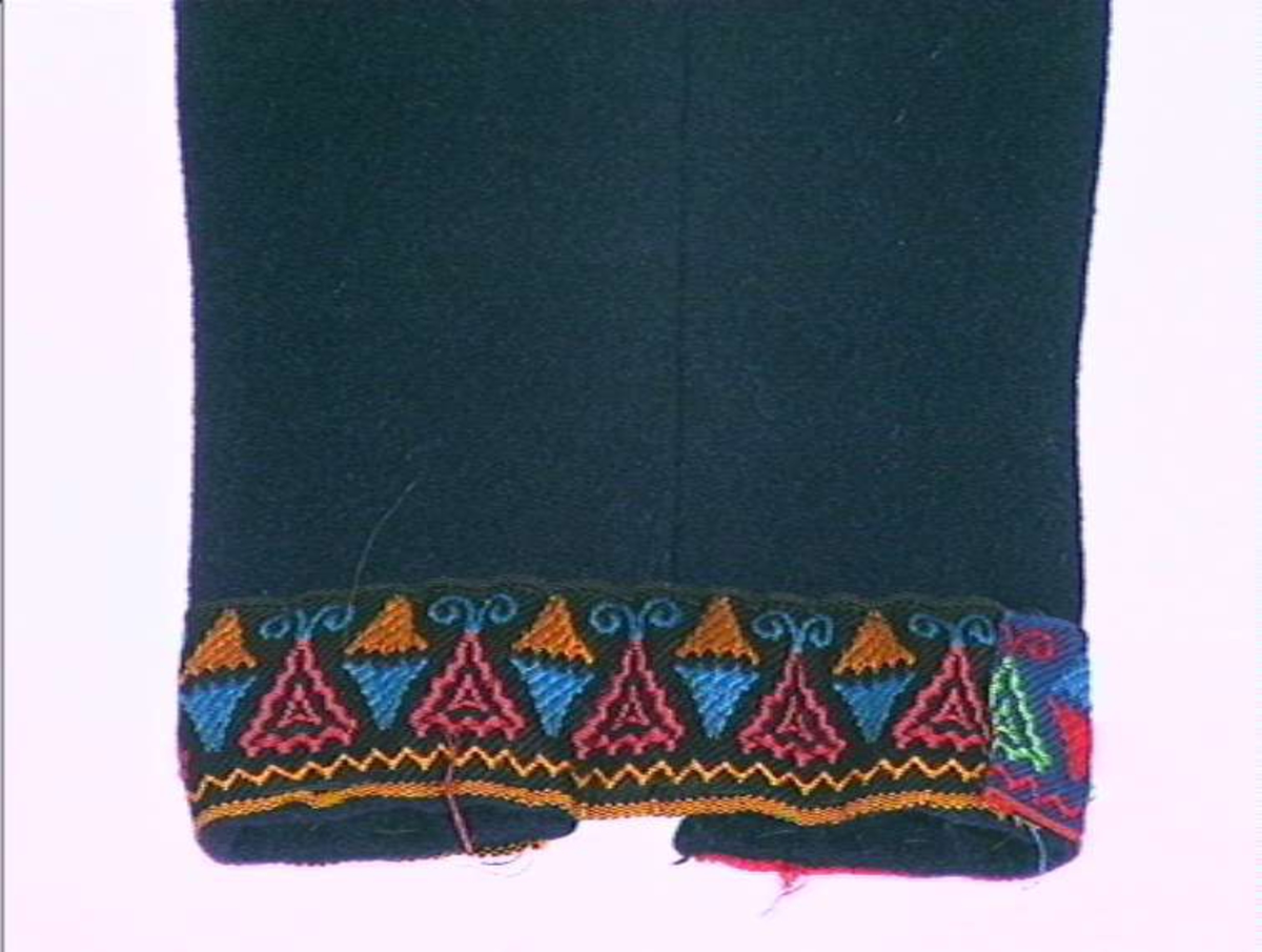 Mørkeblå trøye i ull, maskinsydd. Dekor av 3 cm brede bånd langs fremkanter, hals og ermeringning.I rygg nederst er det 3 innfeldte trekanta kiler som er foret med linlerret og bomullsstoff.