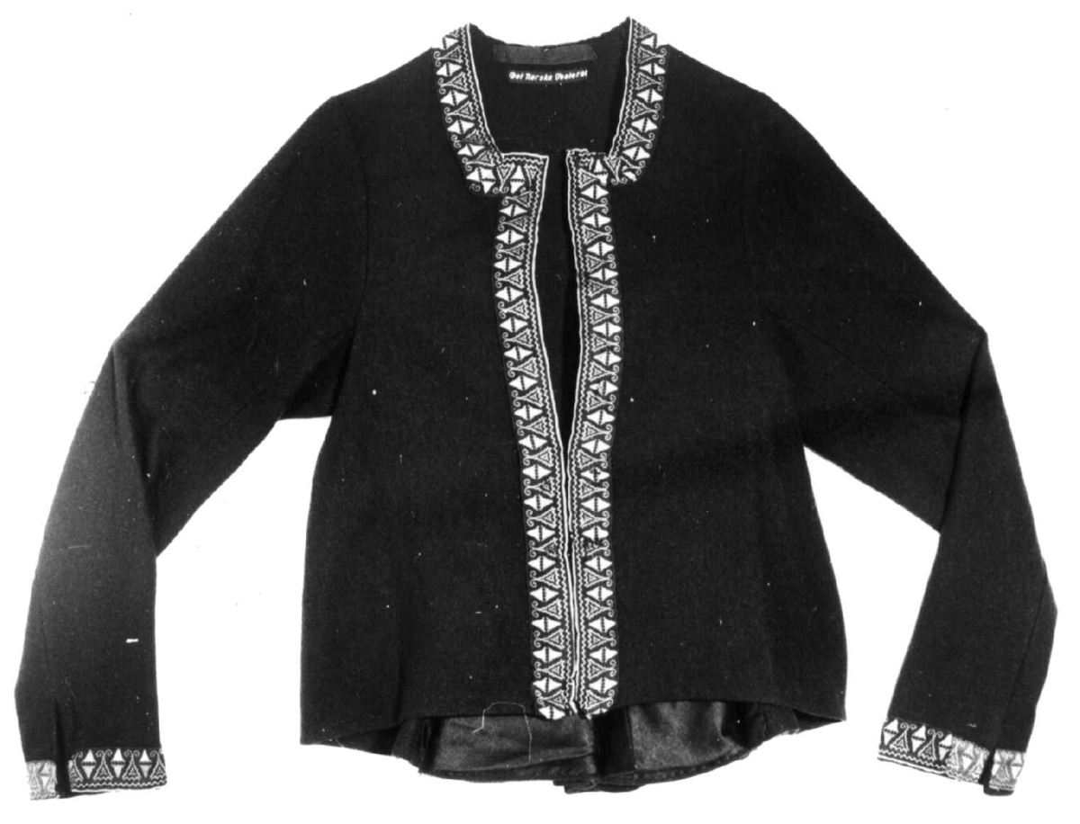 Mørkeblå trøye i ull, maskinsydd. Dekor av 3 cm brede bånd langs fremkanter, hals og ermeringning.I rygg nederst er det 3 innfeldte trekanta kiler som er foret med linlerret og bomullsstoff.