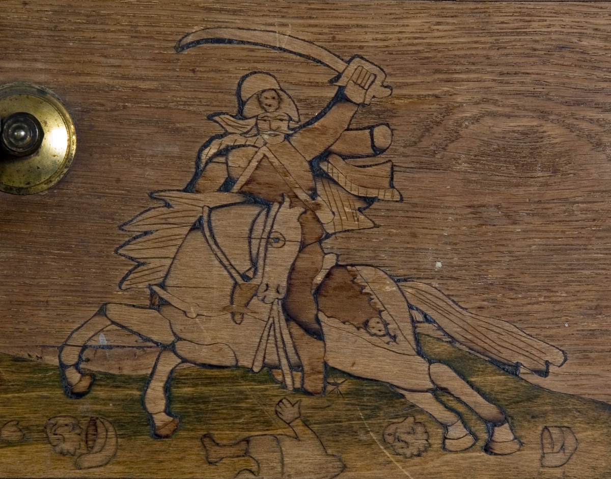 Dragkiste i tre deler med fem skuffer, hvorav en i bunndel. Omfattende intarsiadekor.