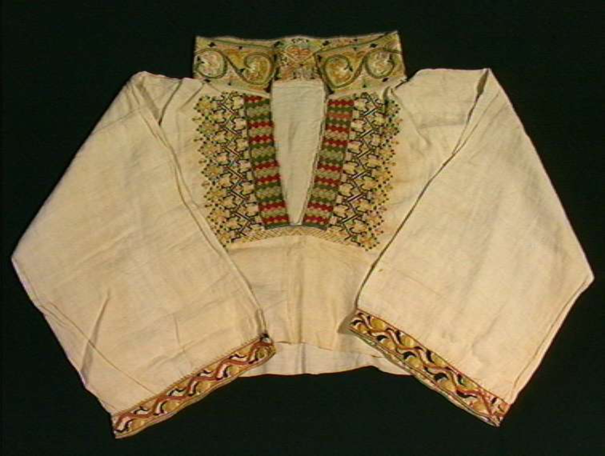 Skjorte fra Sauland, Hjartdal. Broderi på bolen uttrekksøm, klostersøm og korssting. Halslinning og slengerm sydd i plattsøm 
Halskvarde (halslinning) mål:  7,7cm.x57cm ca. Broderi 6,8cm.
Broderi på skulder ca 5,5x6,5cm. 
Brodert bord på slengerm 4cm., avslutning knapphullskant og attersting.