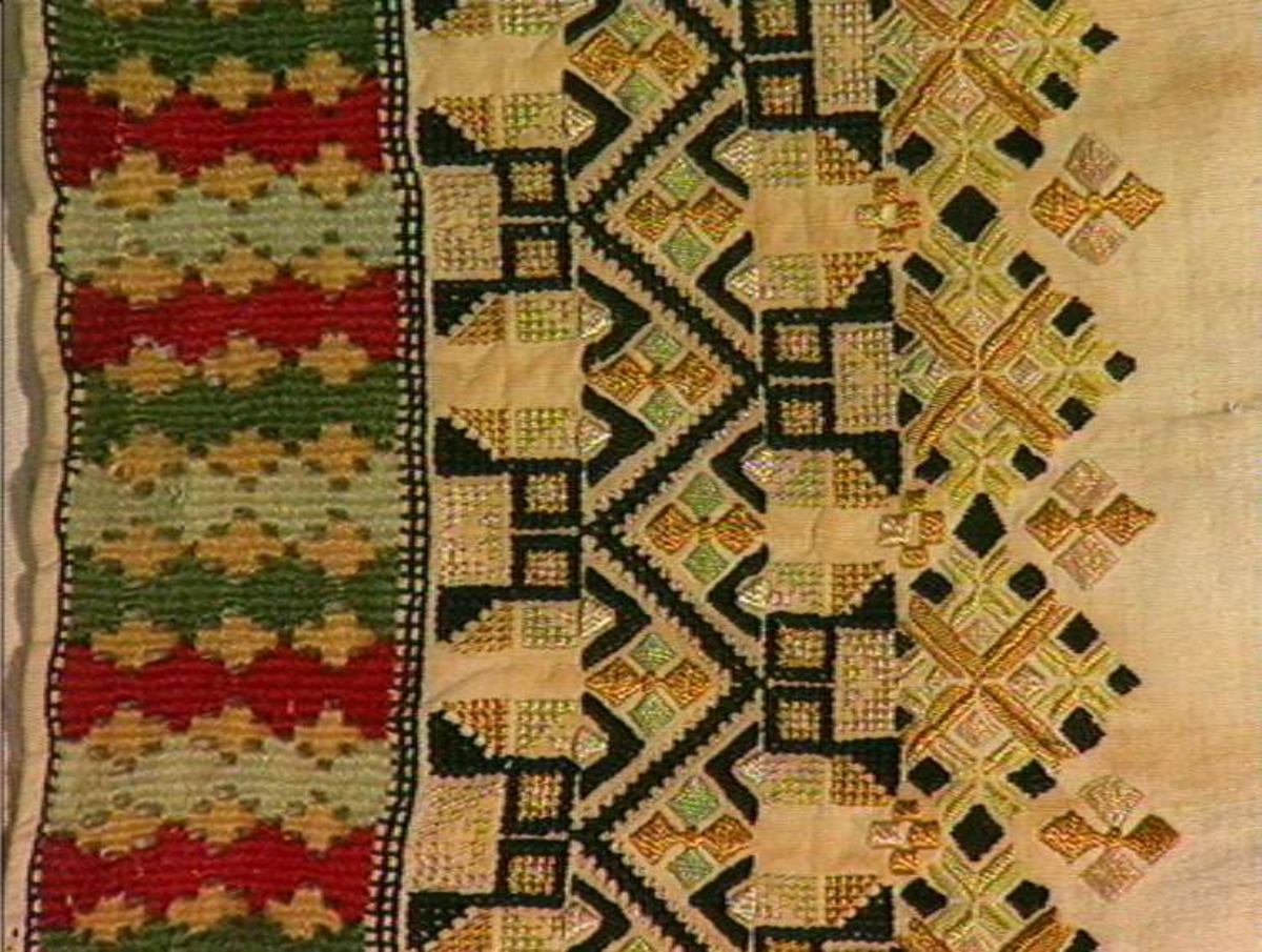 Skjorte fra Sauland, Hjartdal. Broderi på bolen uttrekksøm, klostersøm og korssting. Halslinning og slengerm sydd i plattsøm 
Halskvarde (halslinning) mål:  7,7cm.x57cm ca. Broderi 6,8cm.
Broderi på skulder ca 5,5x6,5cm. 
Brodert bord på slengerm 4cm., avslutning knapphullskant og attersting.