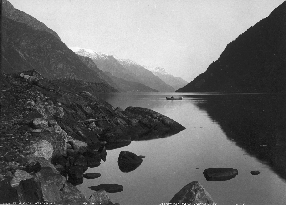 Landskap, utsikt fra Odda utover Sørfjorden. Fjordarm med fjell omkring. Robåt på fjorden.