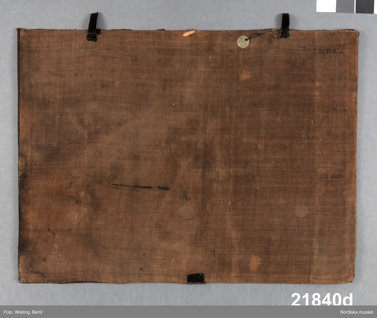 Prydnad till likkista.  Broderad  och monterad på styvt underlag för att hängas på sidan av kistan, med en pendang litt e på andra sidan samt ett mindre med dödskalle och årtalet 1760 , litt c. .
 Bottentyg av mörkbrunt, ursprungligen antagligen svart  tuskaftat ylletyg. Stort fartyg   broderat med silvertråd i olika metallsömstekniker   på ett underlag av pergament för att få reliefverkan  Fartyget som har halade segel är enmastat med gaffelsegel och råsegel  samt  flera försegel på ett långt bogspröt. I aktern den svenska flaggan med applikation av blått sidentyg. Även en toppvimpel med blått siden. Broderiet monterat på en styv pappskiva med baksida av brun linnelärft.  I överkanten två  öglor av svart bomullssammet  för fastsättning på kistan.Troligen är dessa sekundära  Lagningar kring fästet. 
Broderiet är nött och silvertråden svartoxiderad.   Bilderna d och e är identiskt lika men spegelvända.
Förvarades i skepparämbetets i Västerås ämbetskista litt a. 
/Berit Eldvik 2011-08-16