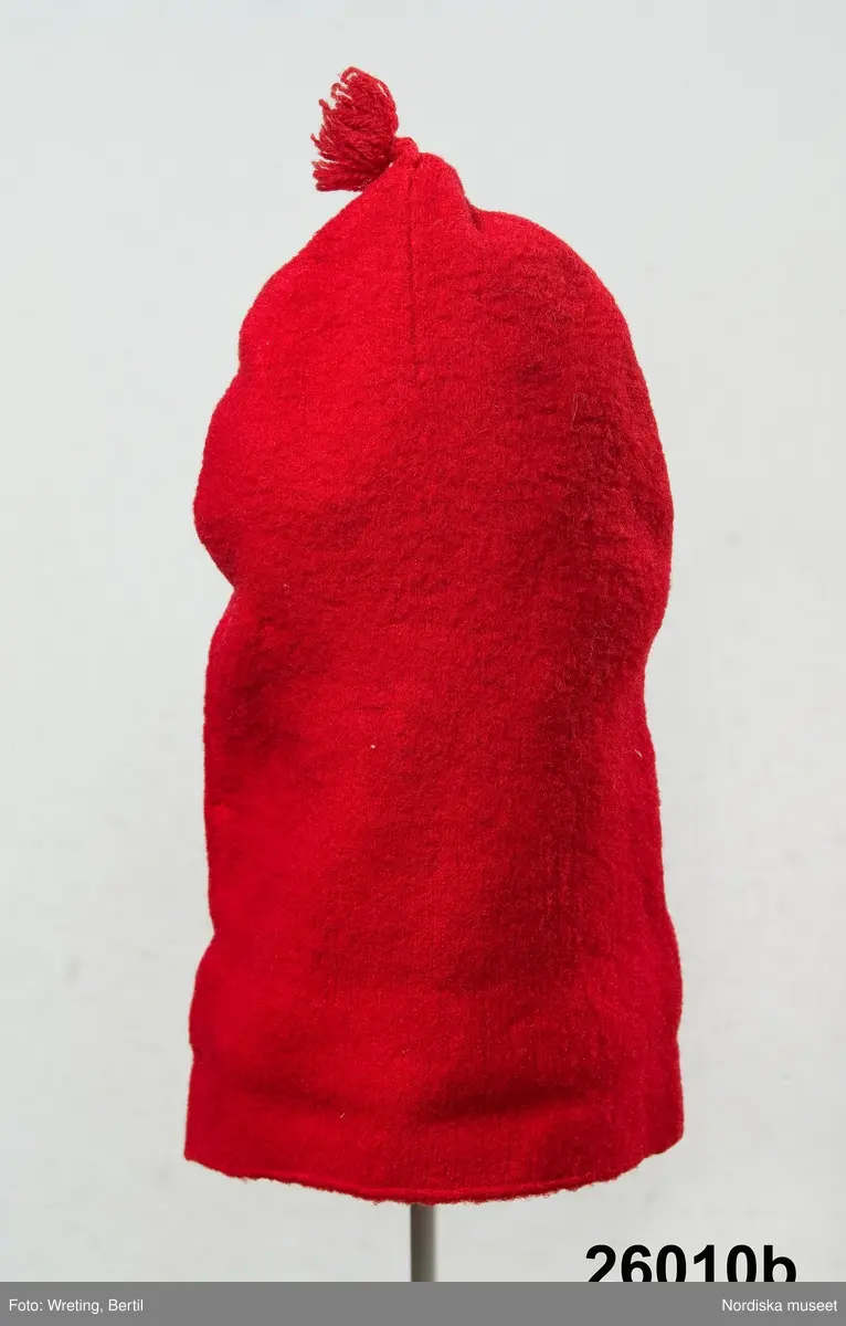 2 st röda toppluvor, A-B.
A.
B.Röd toppluva, maskinstickad i slätstickning av ullgarn, filtad, 2 stycken med nästan osynliga sidsömmar, hoptagningar i toppen. Liten röd ullgarnstofs högst upp. Nederkanten uppvikt 2 varv.

Berit Eldvik okt 2005