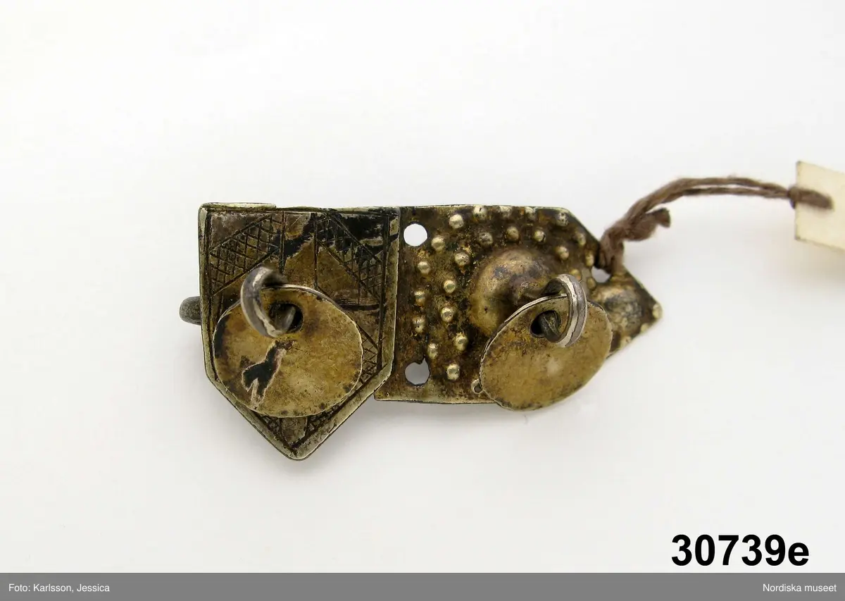 Huvudliggaren:
"a-e, Spännen. från Kalmar län. Af silfver.
Ink. gm friherre Emanuel Cederström [...]. 1/5 1881"

b) "Sölja, silfver, förgyld. H. 3,4 cm, Br 2,5 cm. Stämpel saknas. Frånsidan oförgyld."
c) "Sölja, Silfver, förgyld, gjuten. H 3,6 cm, Br 2,6 cm. Stämpel saknas. Frånsidan oförgyld."

A:1-2 Fyrkantigt halslås, helt förgyllt eller möjligen av mässing, graverad dekor i 1700-talsstil med punsad kant. Fäste för 3 kedjor som alla saknas.
/Berit Eldvik 2007-02-27 