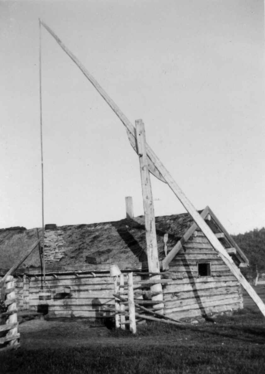 Brønn med vippestang olassert tett inn til en fjøsvegg som det er ført en vannrenne gjennom. Karasjok 1953.