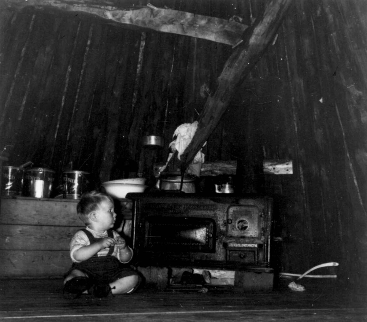 Jonas Thommassons vintergamme, fotografert inne med et barn som sitter ved ovnen. Barbo i Limingen 1956.  