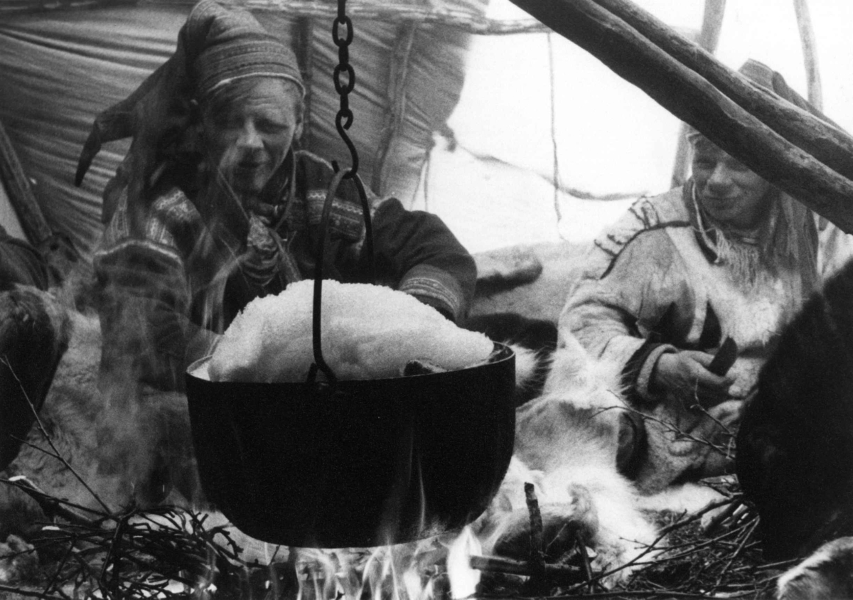 Snøsmelting i telt. To menn sitter ved ildstedet med gryte over. Kautokeino 1957.