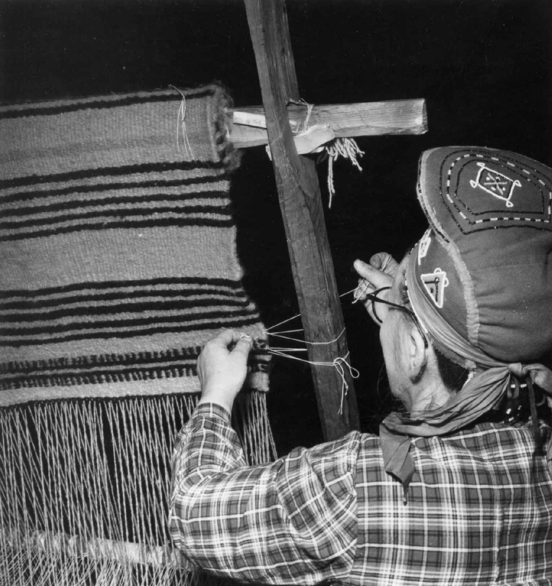 Greneveving. Skoltesamene Darja og Naska Moshnikov demonstrerer grenveveing på Föllisöen, Helsinki Universitet, Finland 1955. 32. Tråden løsnes fra sidestolpene.