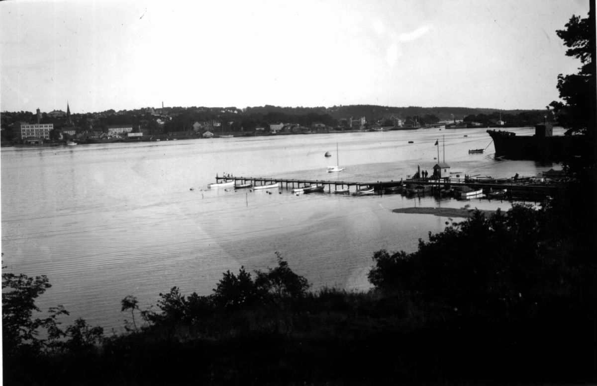 Moss, Østfold. 1930. Oversiktsbilde over Mossesundet. Brygger med båter. Skog. Bebyggelse i bakgrunnen.