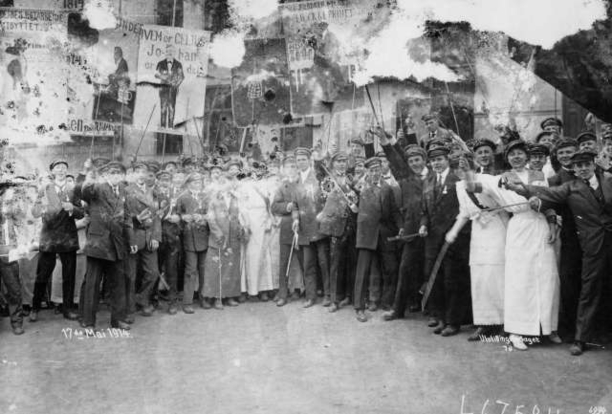 Oslo. Russ 17. mai 1914. Festkledde i lange kjoler og dress. Russeplakater ses i bakgrunnen.