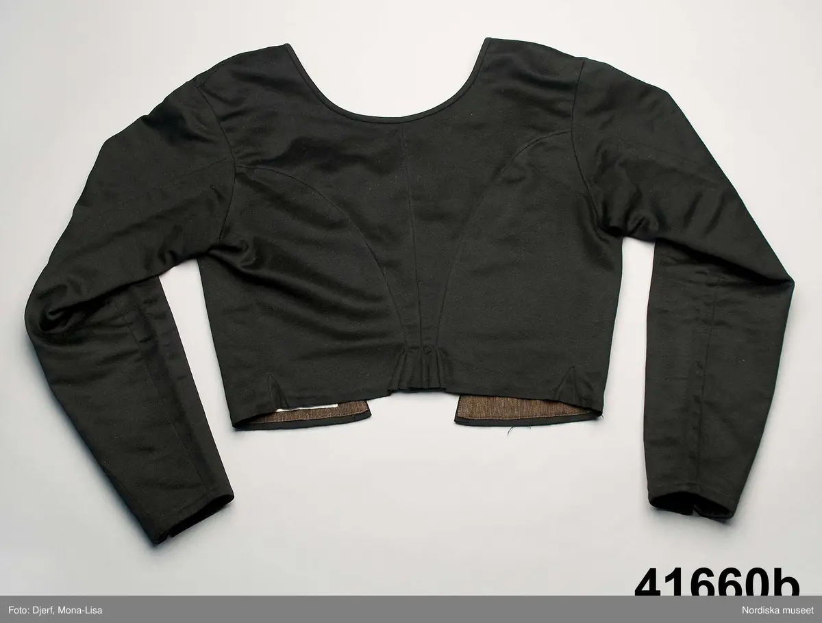 a. Livstyckskjol med liv av grön vadmal och randig halvyllekjol
b.Kvinnotröja, kort modell av svart kläde, med litet skört.
c. Halskläde av rödbottnad kattun
d. Halskläde av röd/gulrutig bomullslärft
e. Kjolväska  av svart kläde med applikationer av vadmal med tenntrådskonturer.
g: 1-4,  mjuk bindmössa av ljusblå sidenbrokad med vita spetsbandsmönster samt blommönster i rosa, mörkrött, vitt och grönt mm.

Dräktdelarna förefaller att vara från något olika tider, och sammansatta för att bli en hel dräkt vid insamlandet till museet. För att illustrera ett äldre dräktskick på orten. 
/Berit Eldvik 2012-02-14