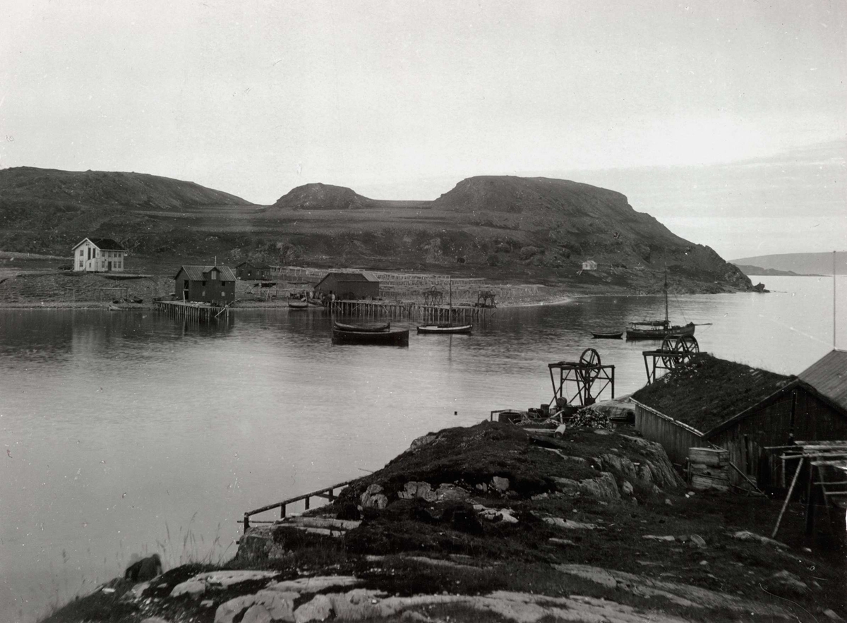 Landskap, Kongsfjord, Berlevåg med utsyn over fjorden med ulike båter og havneparti med kran, sjøbuer og fiskehjell.  Stort bolighus i bakgrunnen.
Del av serie fra en forskningsreise i Øst-Finnmark 1909.