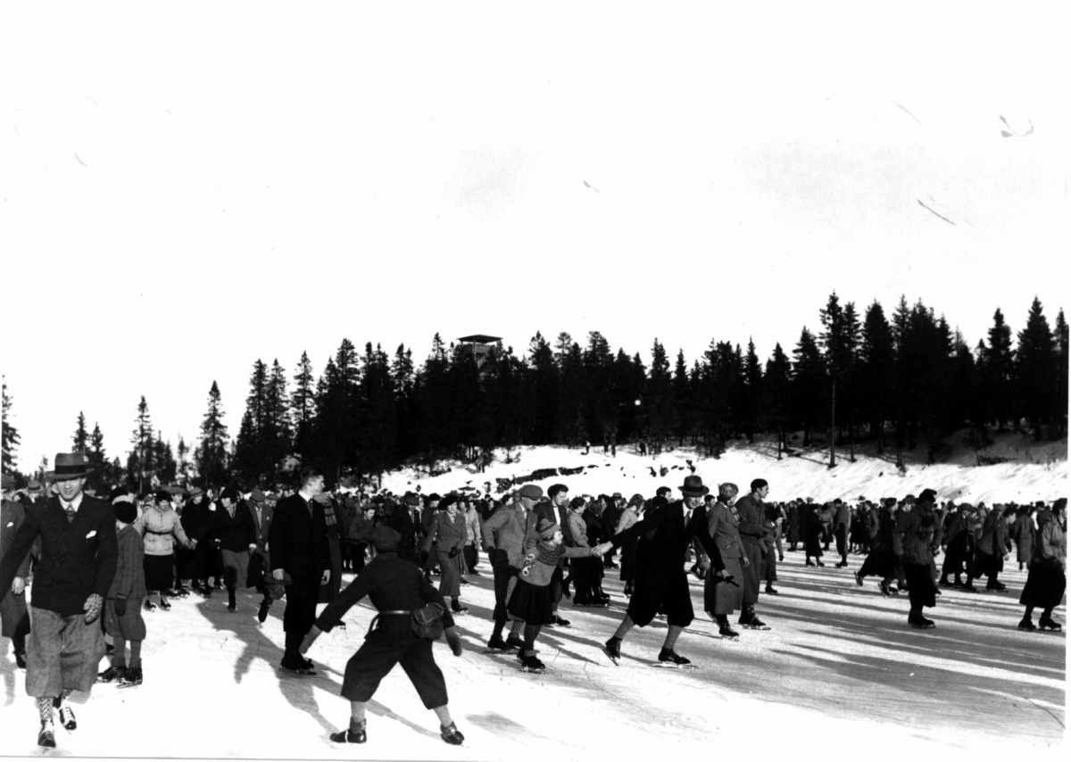 Tryvann skøytebane, Oslo. 1934. Tettpakket med skøyteløpere på isen. Toppen av Tryvannstårnet ses i bakgrunnen.