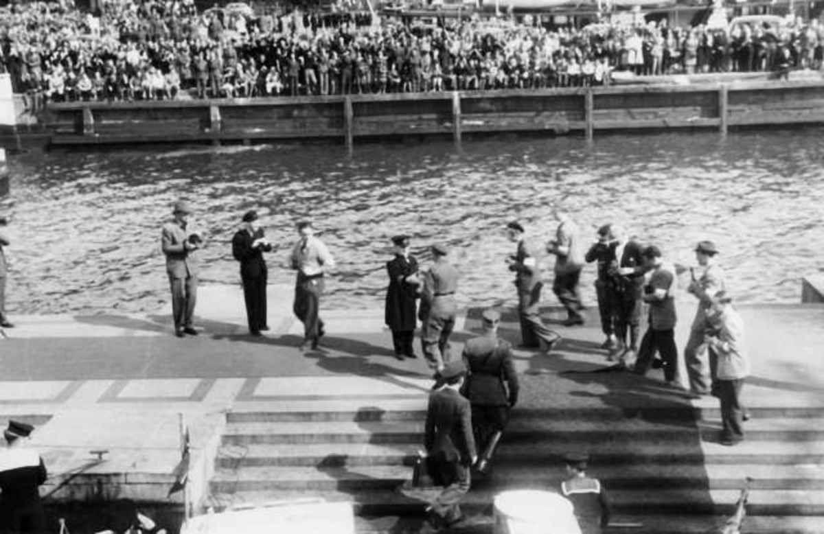 Fra Oslo under fredsdagene i 1945.
Den 13.mai kommer Kronprins Olav tilbake.Her stiger han i land på Honnørbrygga klokken 16.30, 
i spissen for befal fra
Forsvarets Overkommando, og hilser på havnerådmann Kjellstrup. Begivenheten blir behørlig fotografert.