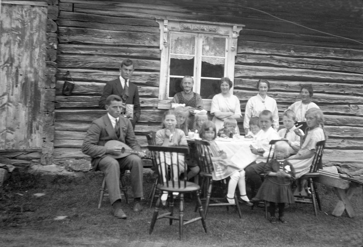 Fritjof Arentz spiller mandolin, Åge Falkanger står bak mot veggen til hytta sammen med noen kvinner. Barn sitter rundt et bord. Trøan ved Røros.