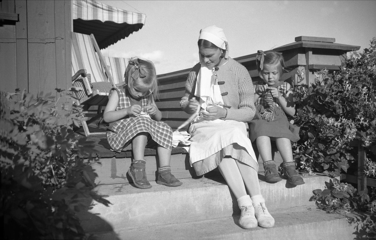 Guri og Siri sitter ute og strikker sammen med barnepleier på terrasse. Fotografert 1935.