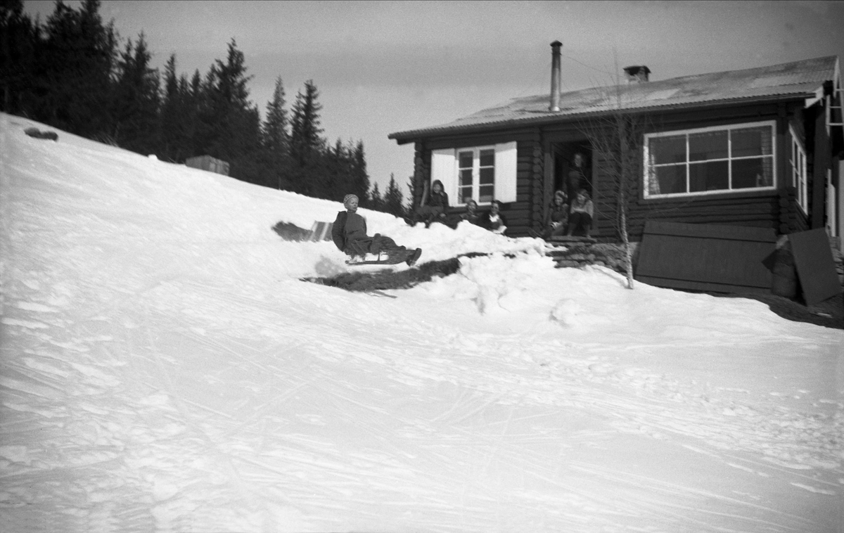 Vintermotiv. Påsken 1944 på Ligardshaug. Voksne og barn sitter i solveggen.