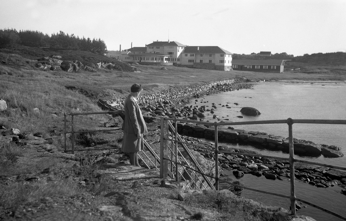 En kvinne står ved nede ved sjøen, tur til Haugesund og Stavanger. En bygning i bakgrunn. Fotografert 1946.