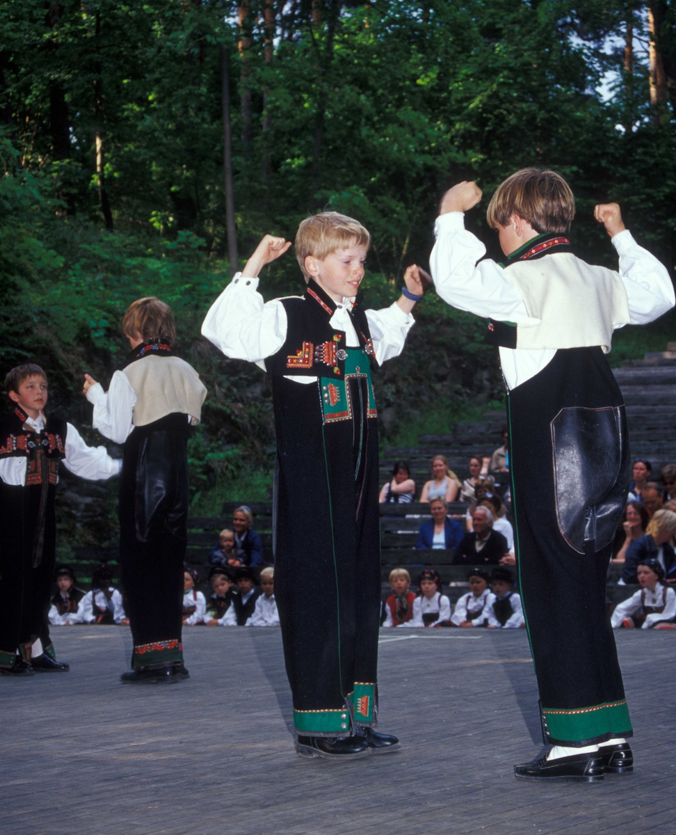 Norsk Folkemuseums dansegruppe, kledd i folkedrakter, danser folkedans i friluftsteateret NF 349. To gutter i forgrunnen.