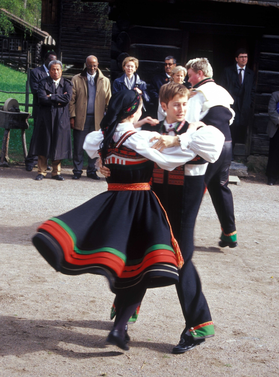 Norsk Folkemuseums dansegruppe, kledd i setesdalsdrakter danser folkedans i Numedalstunet på Norsk Folkemuseum. Et par danser  i forgrunnen mens publikum ser på.