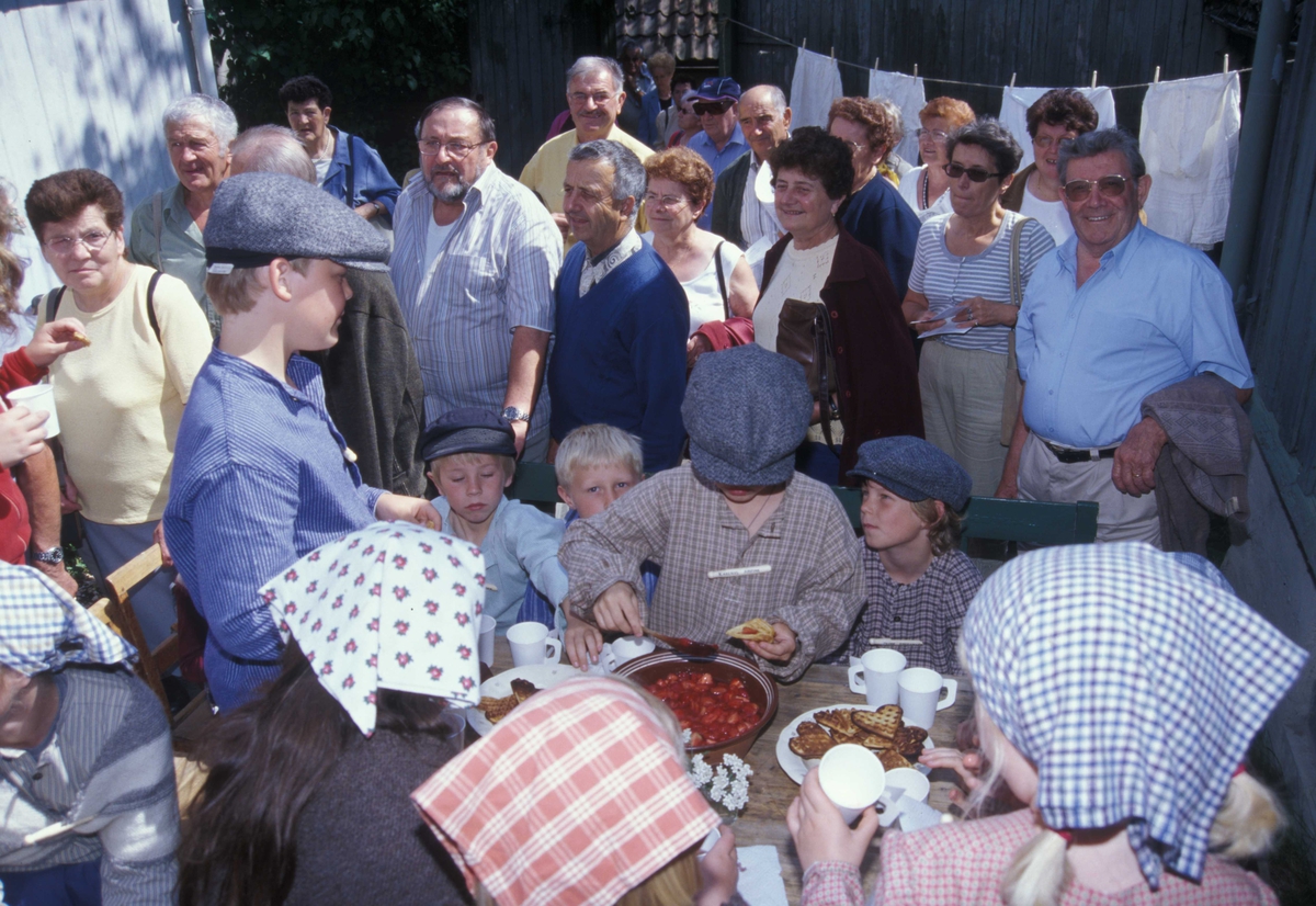 Levendegjøring på museum.
Fra Ferieskolen august 2004.
Samling på Enerhaugen, på Norsk Folkemuseum, med vafler med jordbær.Flere publikumere er på besøk, og står og ser på.
Norsk Folkemuseum, Bygdøy.