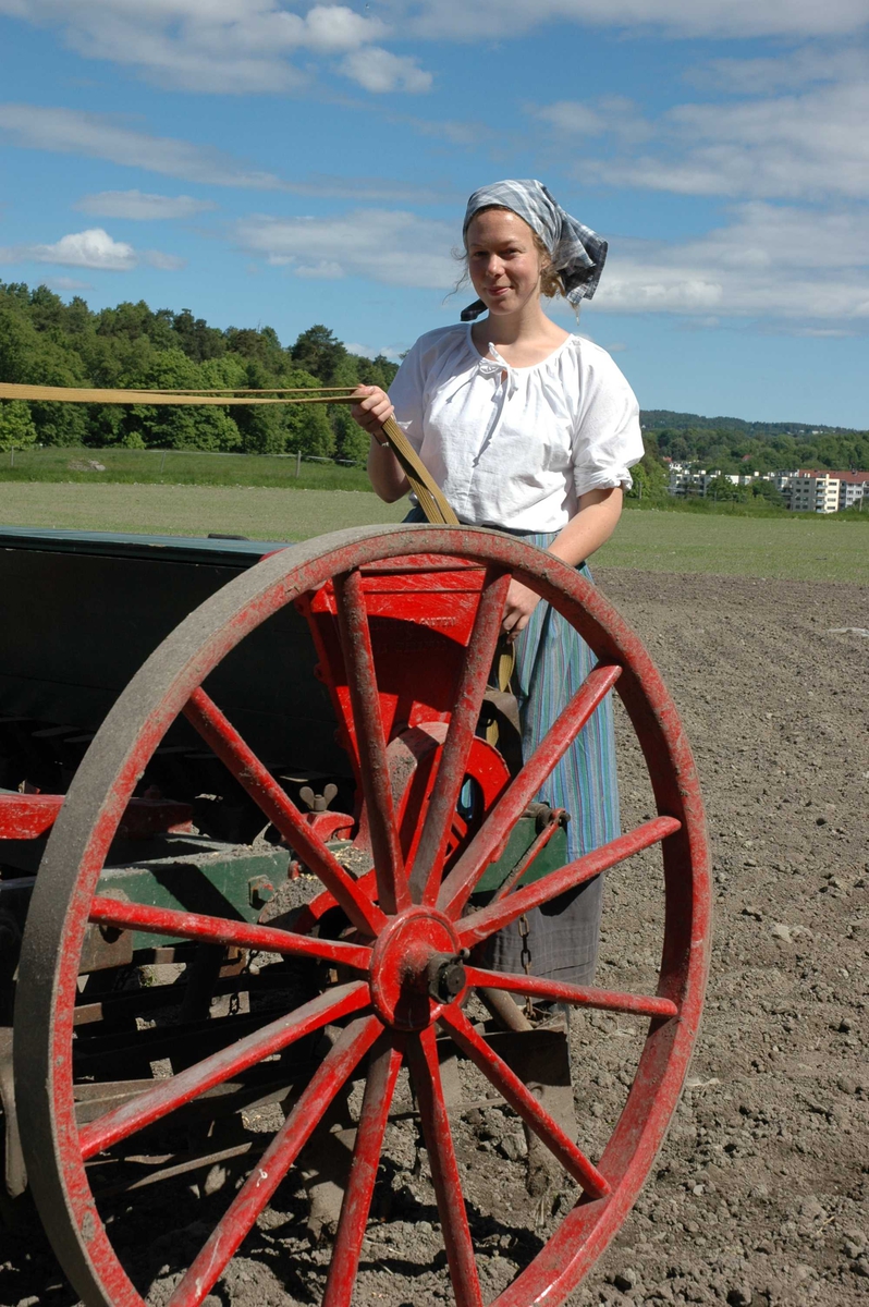 Vert i drakt, Ida Løkken ved såmaskinen på Kongsgården i juni 2005. Det blir sådd bygg.