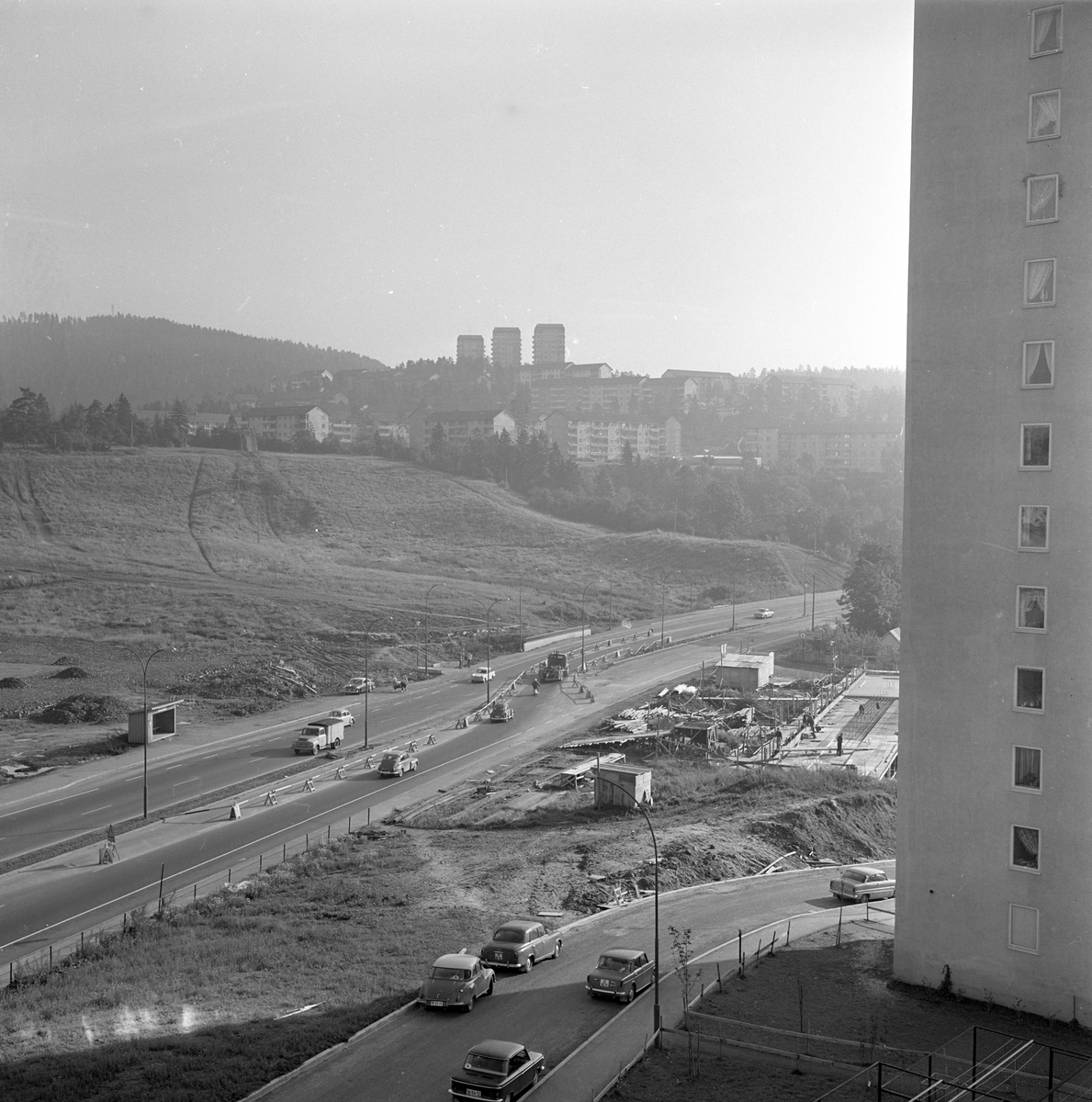 Trafikk på Riksvei 50 med boligblokker i bakgrunnen. Anleggsarbeider i forgrunnen. Fotografert august 1963.