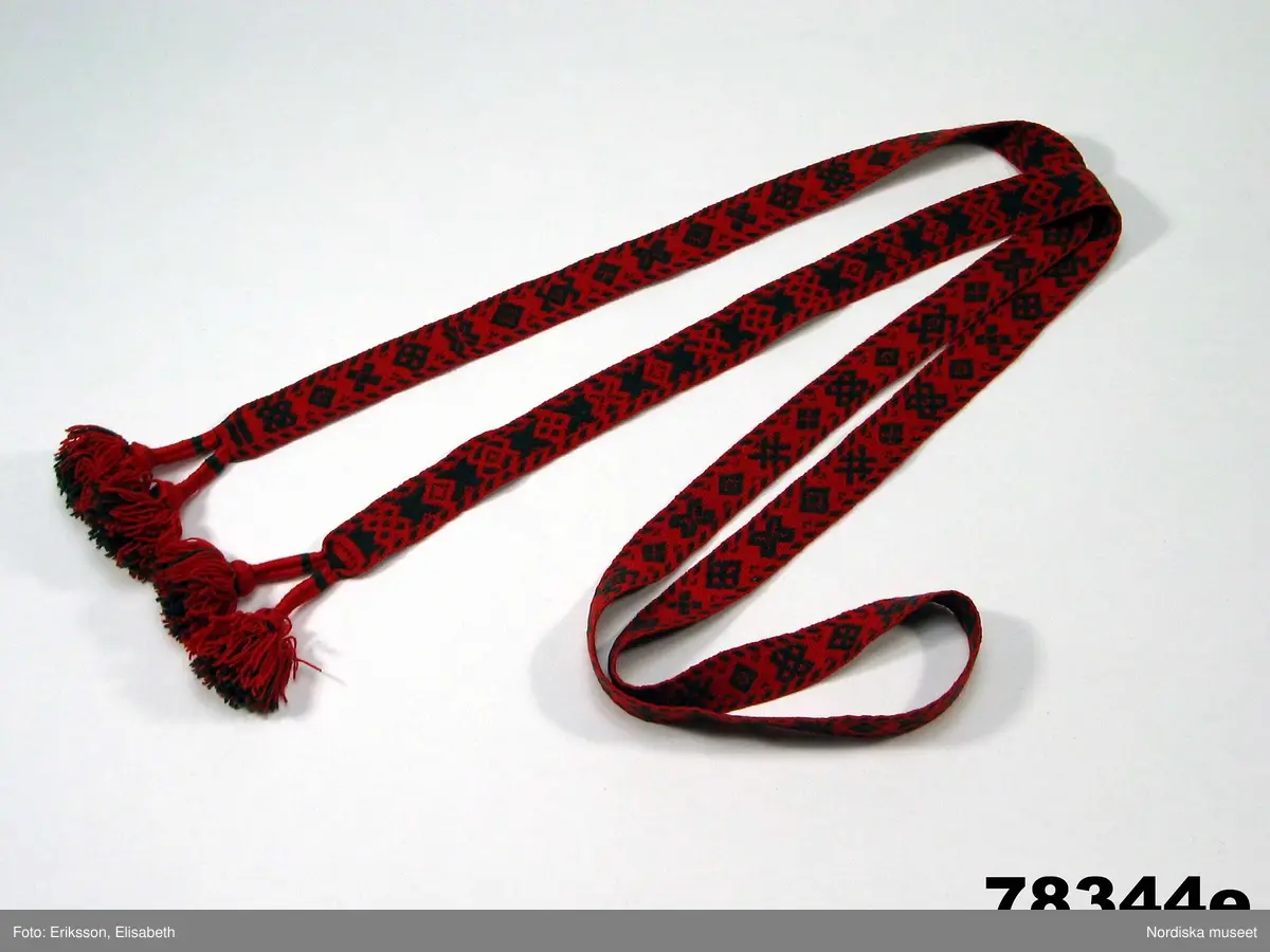 Huvudliggaren:
"Kvinnodräkt fr. Delsbo sn, Norra Helsinglands fgd, Helsingland.
a. "Ryntjeskjortel" af svart kläde med röd kant och bandväfd "kval" (linning). Kjolen "lurad"(goffrerad), skall förvaras lurad att ej vecken gå ut. 3 par fruntimmershänder hjälpas åt att "lura" den efter hvarje begagnande.
b. livstycke, rött med gröna ränder.
c. "Ryntjessärk" (rynksärk) af hvitt bomullstyg med "krus" (handbroderi) kring hals och händer.Begagnas sommartiden
d. "Bumsförkläde" af ylle, blårandigt med bandväf,"kval" i rödt och grönt.
e. "Förklesband" rödt och grönt ylle med "doppar" (tofsar) i ändarna. Lindas 1 à 2 hvarf kring lifvet och bindes framtill med stora nedhängande "locor" och ändar. Längd 262 cm, bredd 3,4 cm.
f. Kjolsäck med mässingslås och hake samt tennbroderi. Häktas under förklesbandet och hänger delvis under "försklet". Begagnas vanligen till förvaring af kyrkkryddor m.fl. kyrk-ellerkalassaker.
g. Halfhandskar af svart kläde med silkesbroderi. Begagnas sommartiden.
h. "Påshufva" hvardagsmössa af brokigt kattun. Begagnas med i nacken utslaget hår med några hårtestar hängande fritt framför öronen.
Till dräkten användes röda strumpor samt låga skor med höga klackar. Äfven kan användas silfersmycken kring halsen eller å  bröstet. En á två brokiga silkesdukar brukades omkring halsen nedstoppade under lifstycket, så att kruset kring halsen  på "ryntjessärken" sammanfästadt med ett löfspänne samt en smalare kant af hvarje sidenduk, blevo synliga. Vid handlederna sammanfästes ryntjessärken med röda sidenband eller länkknappar.

a. KJOL 
längd: 87 cm
midjeband bredd: 7 cm
av svart halvylle med svart linvarp och inslag av svart 1-tr. ullgarn, de 2 yttersta stadtrådarna är av oblekt lingarn. 4 goffrerade våder samt en slät framvåd som skarvats under förklädet med oblekt bomullslärft. 5 cm bred list av rött kläde i nederkanten runtom. Brett midjeband mönstervävt i rött och grönt ullgarn och vitt bomullsgarn. Knäppt vid framvådens vänstra sida med 2 hakar och hyskor av mässing.
b. LIVSTYCKE
längd: 39 cm
av halvylle i varptäckande kypert, varp av vitt lingarn, inslag av svart och grönt ullgarn med flaminslag av vitt, 2 fram-och sidstycken, 2 bakstycken avsmalnande till skörtveck med tre par tränsade förstärkningar av svart garn. I midjehöjd ett avsytt veck runtom, knäppt kant i kant med 8 par grova hakar och hyskor av mässing. Foder av ofärgad bomullslärft.
BE

c. ÖVERDEL
Längd: 39 cm. Längd: 58 cm - ärmlängd. Vidd: 56 cm - ärmvidd. Vidd: 114 cm. Höjd: 1,7 cm - kraghöjd. Material: Textil, bomull. Textil, linne - ärmlinning, krage. Bomullsgarn - broderi. Telnik: Tuskaft. Trådbundet broderi. Broderi, rätlinjig plattsöm. Handsömnad.
Överdel av tuskaftat vitt bomullstyg. Dubbelvikt bålstycke, isydda rektangulära halsspjäll. Täta breda stripade  rynkor mot halskrage i bomull, 1,7 cm hög. Kragen har broderier i rätlinjig plattsöm, vitt bomullsgarn över hela ytan, nuggor i kanten, langetterade bågar  i framkant. 16 cm långt sprund fram, tränsad förstärkning nedtill, 3 cm.  Vidsydd ärm med  infällda ärmspjäll, lagda veck över axeln fram och bak. Täta breda stripade rynkor mot 2,5 cm bred ärmlinning. Ärmlinningen har yttäckande vita broderier i rätlinjig plattsöm, rombiska former. Vita knytband i bomull i ärmlinningar och krage. Överdelen är handsydd.
/Inga-Lill Eliasson 2007-11-26


d. FÖRKLÄDE
längd=vådbredd: 82 cm
bredd: 97,5 cm
av halvylle, varp av svart lingarn, inslag i varptäckande kypert av svart 1-tr. ullgarn med smala ränder istarkt blått och en knappt synlig svart tråd med vita flamgarnsfläckar av bomull. Upptill stripade rynkor där de blå bårderna utnyttjats dekorativt i rynkningen. Mönstervävt midjeband i grönt på rött ullgarn , bandet knäpps med 2 hakar och hyskor i vänster sida.
I nederkantens båda hörn infodringar på insidan av svart bomullslärft, för att tyget inte skall rulla sig.



Berit Eldvik 2004