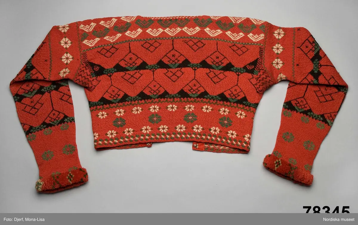 Kvinnotröja, midjekort, slätstickad i hårt tvinnat tunt ullgarn, helt mönstrad i rött som dominant färg, samt svart, grönt och vitt. Det vita garnet är bomullsgarn, vilket föredrogs för att det gav en renare vit färg än ullgarn. Mönstret är specifikt för socknarna Delsbo och Bjuråker. Stickningen utförd så att trådarna binder hela vägen på baksidan. Bålen rundstickad och sedan uppklippt mitt fram, där öppningen kantats med rött kläde. Fyrkantig halsringning infodrad med oblekt linnelärft. Knäppt med 5 par hakar och hyskor av mässing. Ärmarna stickade för sig och vidsydda mot bålen. Ärmarna avsmalnar mot handleden där de kantats med ett flossabräm av  ullgarn i rött med mönster i grönt och vitt. Brämet vävt med botten av lingarn och inknutna nockor som sedan klippts kort och jämnt.
På bröstet instickad märkning I S S D  1 8 4 4 = jungfru Sigrid Svensdotter.
Dessa tröjor blev moderna kring 1830-40 tal i Delsbo och användes som söndagseftermiddagsdräkt framförallt av de unga som då samlades till dans eller andra nöjen. Männens tröjor var av samma slag men var inte öppna fram.
/Berit Eldvik 2007-07-03