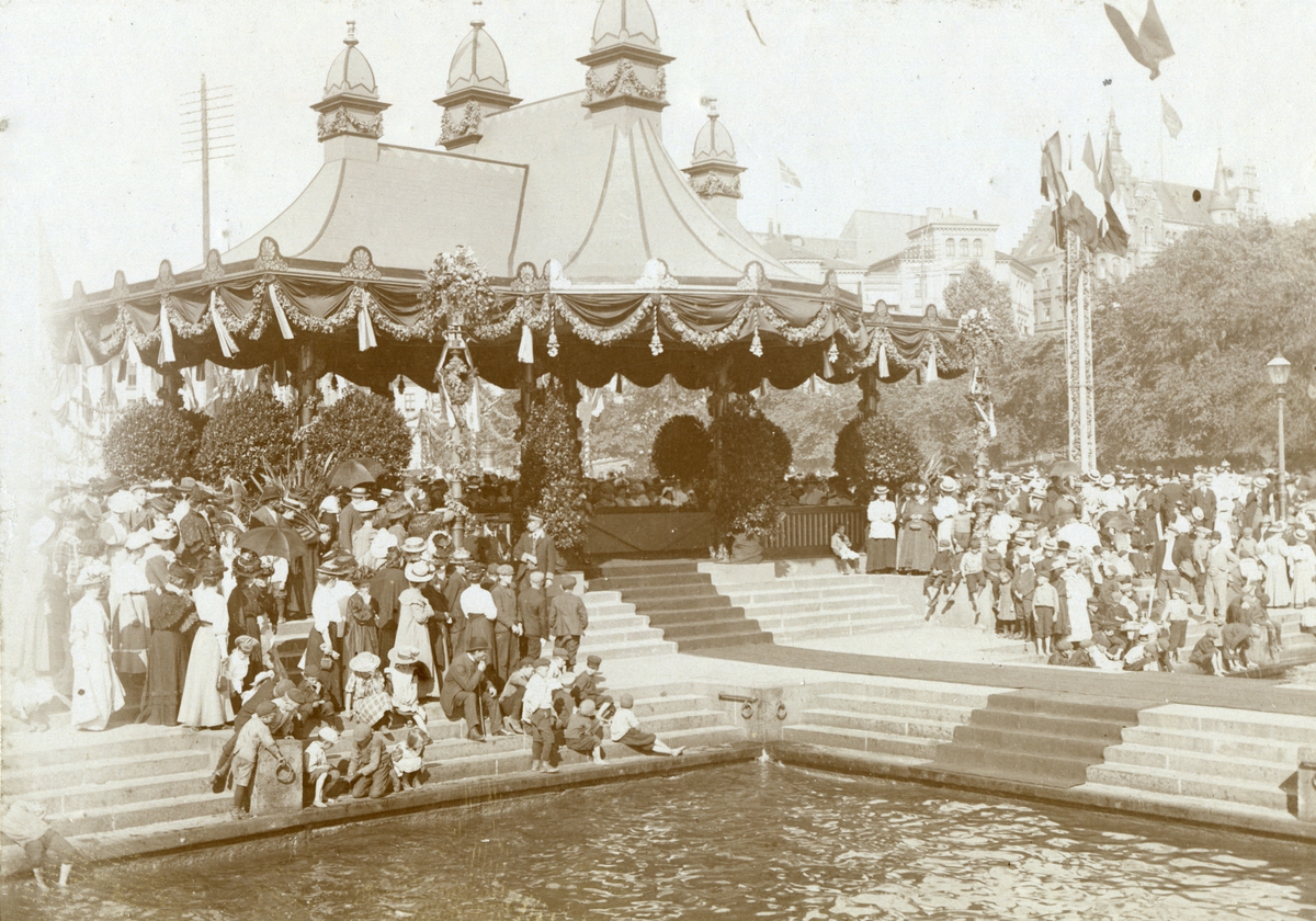 Serie med fire foto fra den franske prsidenten Clement Armand Fallières statsbesøk i Kristiania i 1908. Velkomstpaviljong med baldakin, pyntet med girlander og flagg. Dekorasjoner utført av B. Lange, antakelig. Tilskuere på Honnørbrygga i hovedstaden. Karl Johans gate er også pynytet med dekorasjoner.