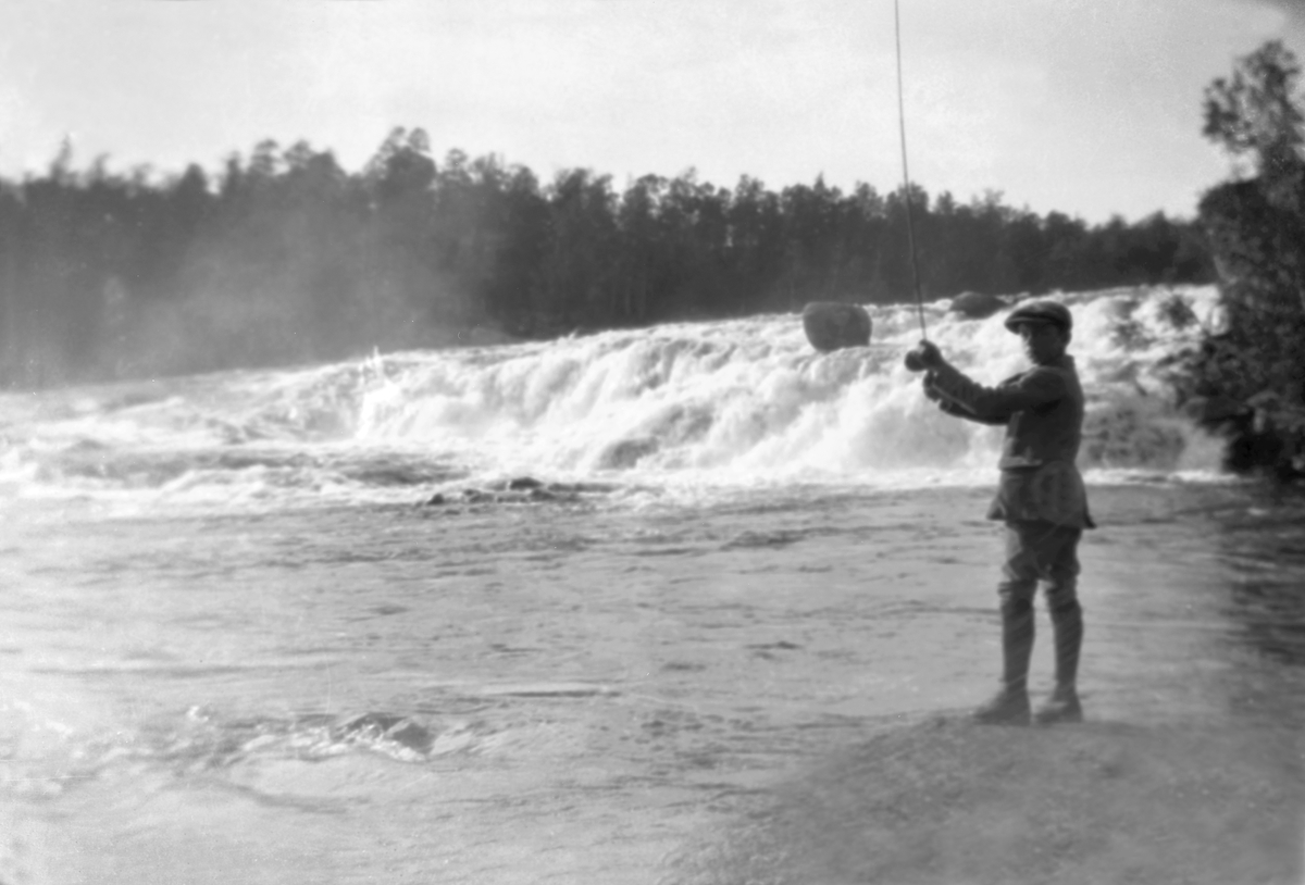 Bjarne Arentz står på bredden av Glomma og fisker med stang. Fotografert ca. 1912-13.