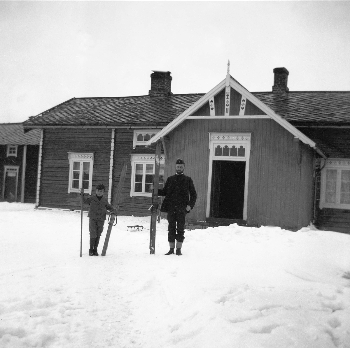 Mann, antagelig sanitetskaptein Bjarne Arentz, og gutt med ski uten for våningshus.