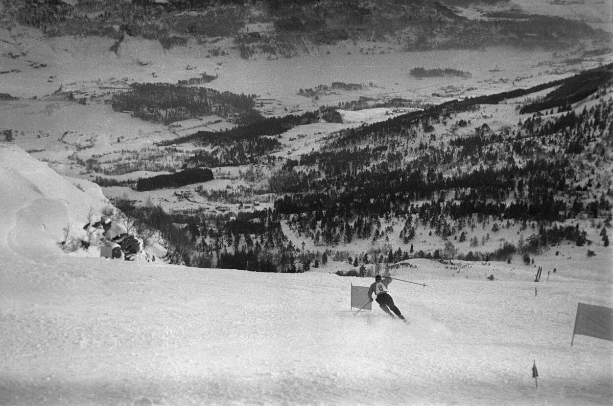 Oversiktsbilde over Voss. En alpinist med startnummer 19 på brystet i fin stil gjennom portene.  Holmenkollrennene på Voss 1952. Fotograf Dagbladet