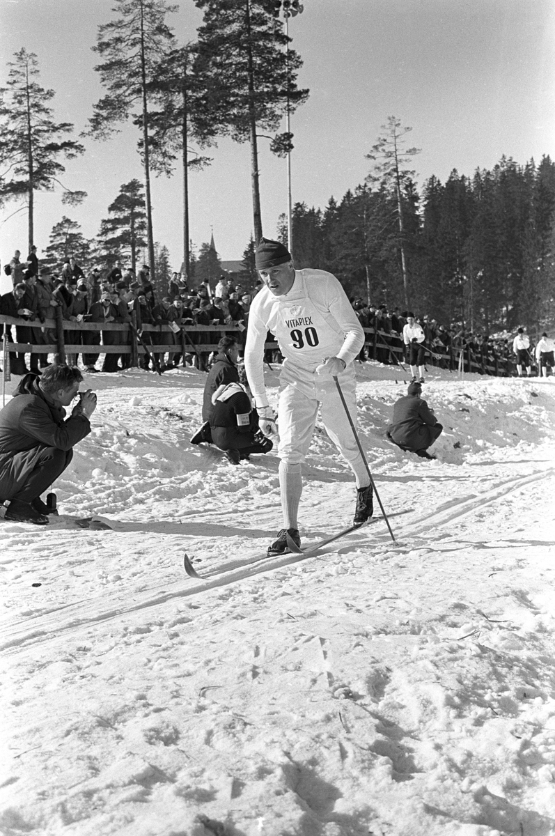 Skiløper med startnummer 90 i Holmenkollen. Publikum langs løypa.  Pressefotografer på sidelinjen. Holmenkollrennene 1963.