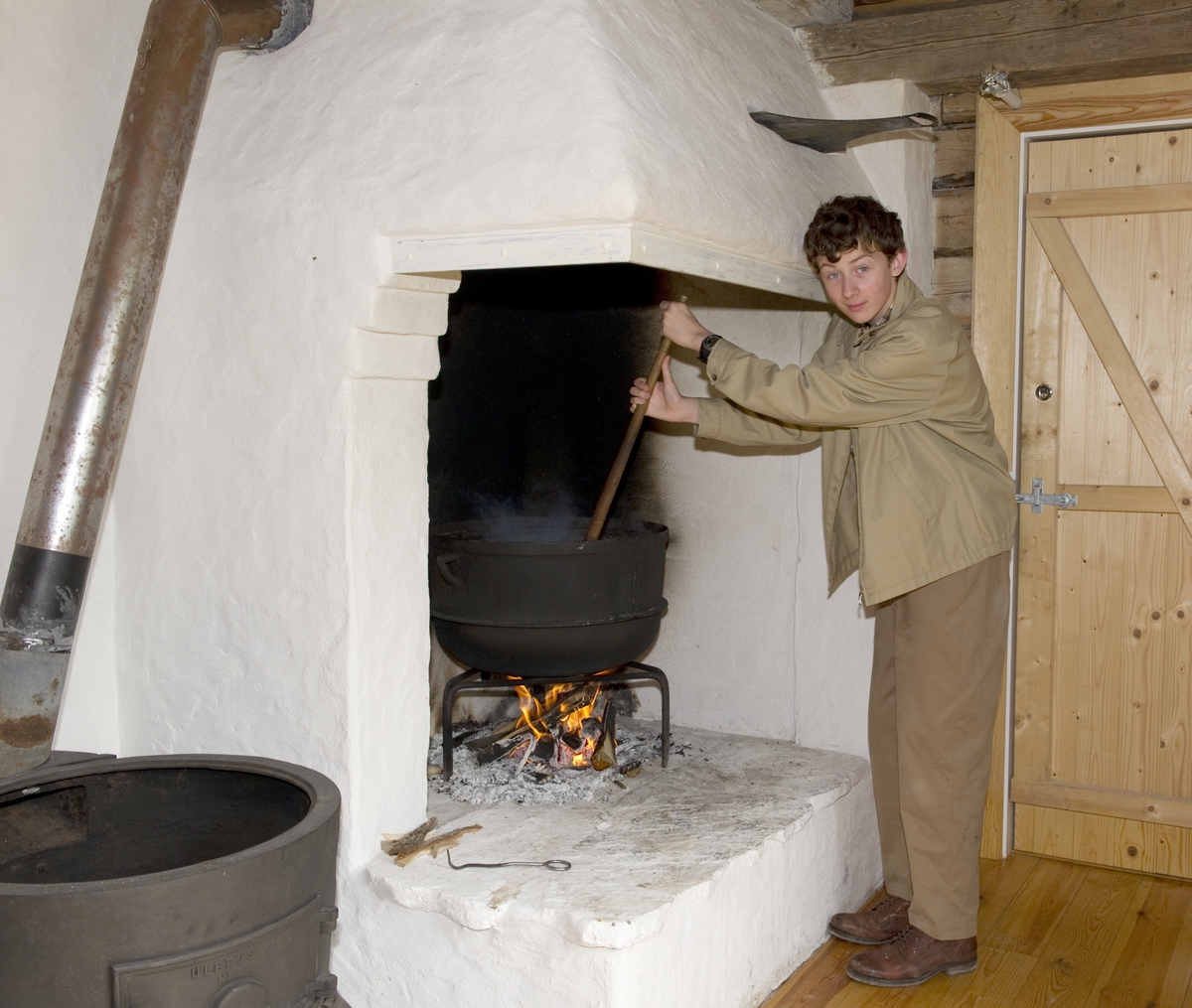 Trønderskolen anno 1959. Norsk Folkemuseums sommertilbud til ungdom. Deltakerne prøver seg på praktiske arbeidsoppgaver som det var vanlig at ungdom deltok på for 50 år siden. Trøndelagstunet på Norsk Folkemuseum. Gutt i arbeid med å røre i gryte i grua.