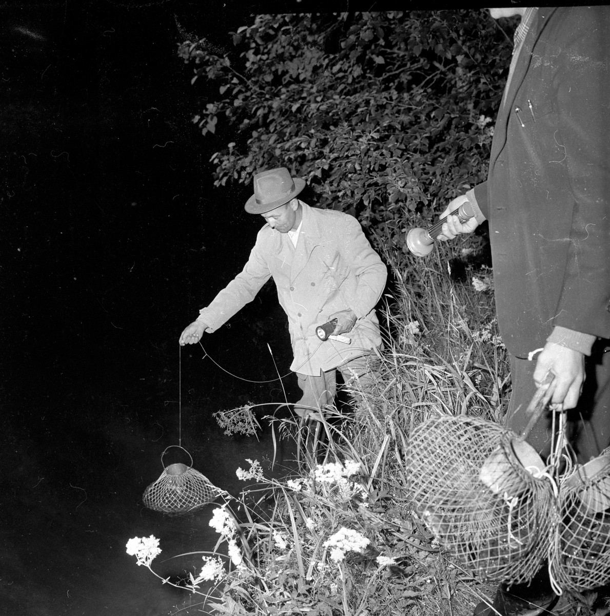 Mann med hatt krepsefisker med teine om natten.
Fotografert 1958.