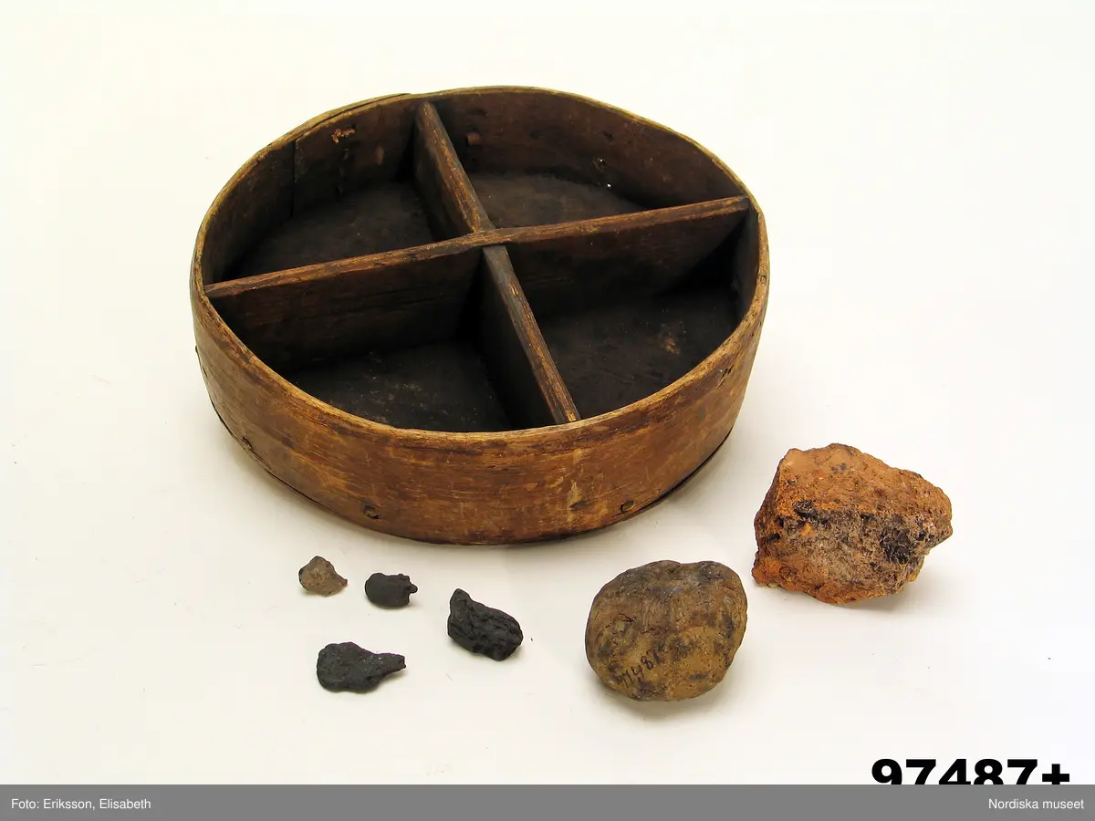 Huvudliggaren:
"+ Trollask med varjehanda inneh. Av trä, rund, delad i fyra fack. Från Bysjötorp. Ink. 31/12 1903 Gm Keyland, N., kand., Stockh. [Brukningsort:] Västmanland Hjulsjö sn. [Insamlingsnummer] 660."

Katalogkort:
"I fyra fack. Innehåller en tegelstensbit, ett litet stycke kvarts, en rund sten, ..."

Lena Kättström Höök 2019-04-26