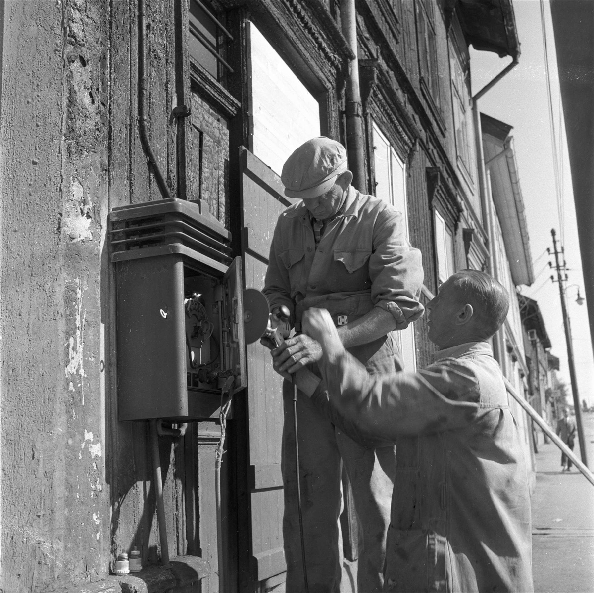 To menn reparerer brannmelderen i Totengata på Vålerenga i Oslo i 1958, etter en tragisk trikkebrann.