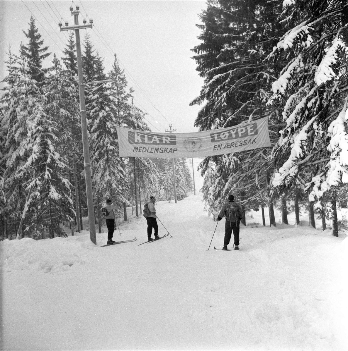 Skiløpere fra Bøler til Ski,  Skiforeningen har hengt opp banner, ønsker flere medlemmer, Oslo, Bøler, 17.01.1959 
