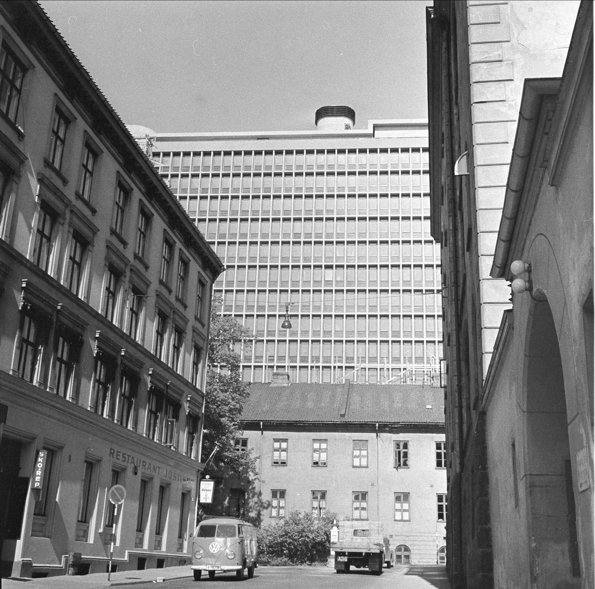 Pløens gate foran Rregjeringsbygget. Justisdepartementets bygning i perioden 1883-1958, til høyre port inn til gårsplassen i Møllergaten 19.
Fotografert i Oslo i  juni 1958. Gatebilde med bygninger og biler.