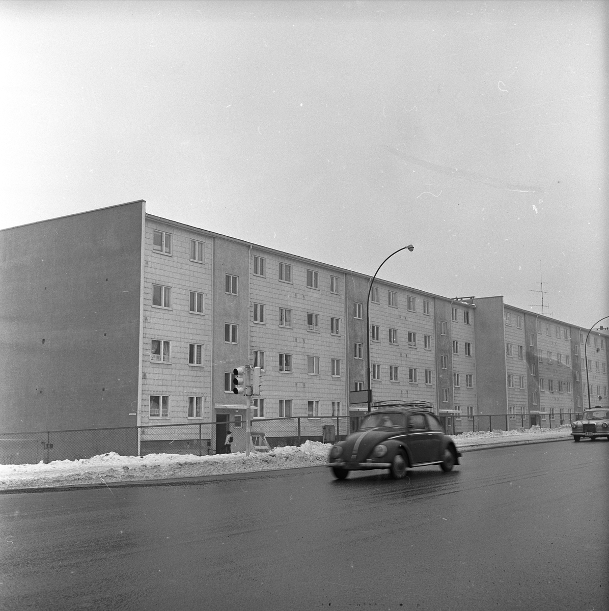 Bil av typen folkevogn WV passerer blokkbebyggelse i Trondheimsveien ved Veitvet i Oslo. Fotografert i 1965.