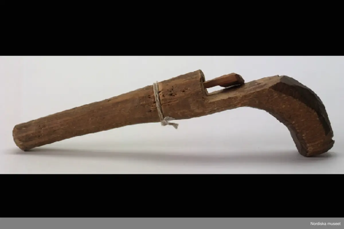 Inventering Sesam 1996-1999:
L 20,B 2,7 cm
Ärtpistol av trä i både pipa och stock. "Påskjutare" att föra in i röret,  tillverkad senare.
Ett vitt bomullssnöre runt pipan liggande i en skåra.
Helena Carlsson 1996